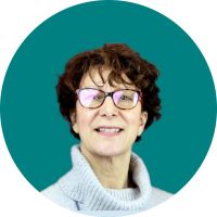 A headshot of Anne Brookes Canalside Life Coach. She has curly short brown hair and is wearing red glasses and a pale jumper.